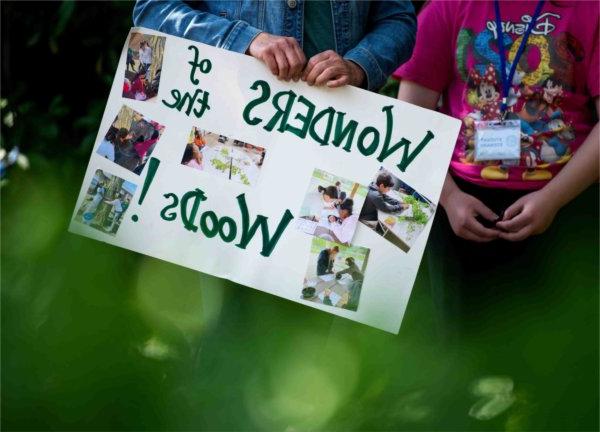 一位老师举着一个牌子，展示他们的学生项目“森林的奇迹”!5月15日，在皮尤大急流城校园举行的Groundswell管理倡议学生项目展示会上.