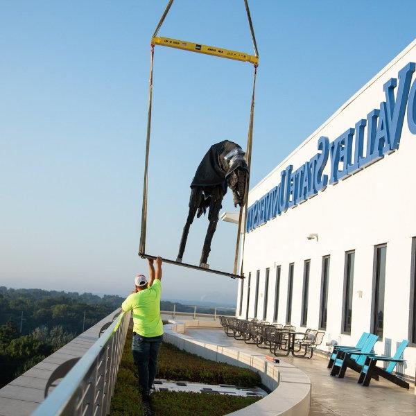 construction workers reach for a sculpture that is hoisted by crane on the terrace of DCIH, Pew Grand Rapids Campus