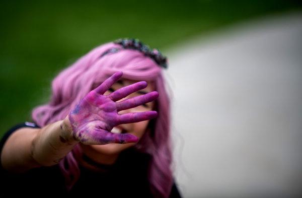 A person reaches their hand out in front of their face showing purple chalk dust covering the surface of their hand