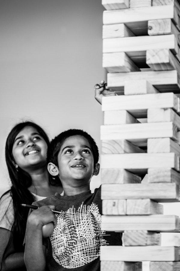  Two children reach toward the top of a tall stack of Jenga blocks