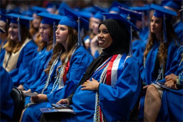  一名毕业生戴着蓝色的帽子，穿着蓝色的长袍，把手放在肚子上.