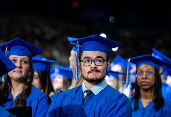  戴着蓝帽、身穿蓝袍的毕业生在听毕业典礼演讲人讲话.