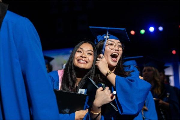  两个毕业生微笑着拿着他们的毕业流苏.